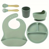 Set of green silicone baby utensils including a bib, cup, bowl, and plate .