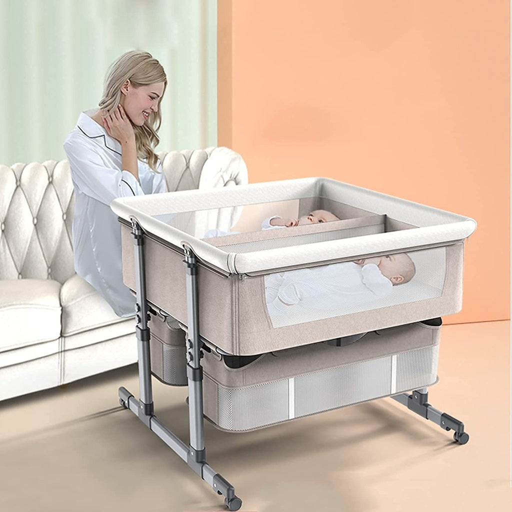 Woman sitting next to a baby in a Twin bassinet portable crib with wheels.