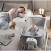 Woman lying on a bed with a baby in a portable baby swing crib .