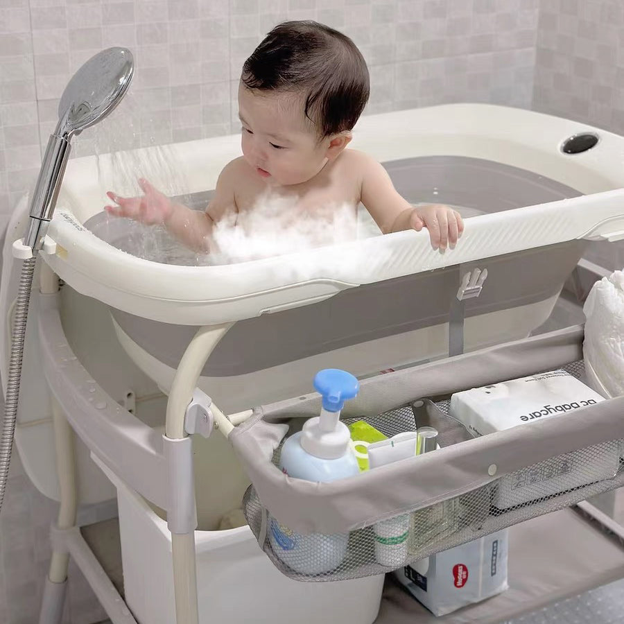 Baby in a 2 in 1 adjustable portable bathtub with a shower head and supplies on a stand.