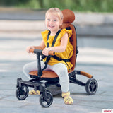 Young child seated in a convertible rider ll brown and black stroller-style tricycle outdoors on a paved surface, featuring a brown seat and backrest, black frame and handlebars, and small black wheels.