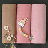 Three rolled-up baby swaddle in brown, pink, and light pink with a baby teether 