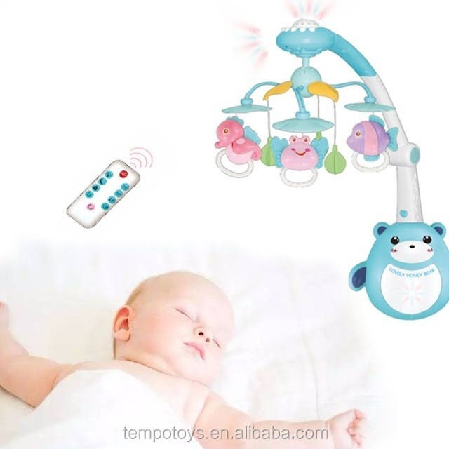 Baby sleeping next to a colorful baby bear bell crib mobile with remote. control