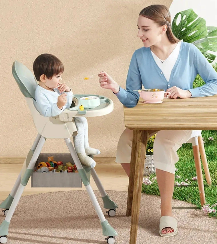 Woman feeding a child in a booster seats high chair in a home setting.