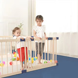 Two children standing behind a wooden foldable playpen, with colorful balls scattered across the floor in front of them.