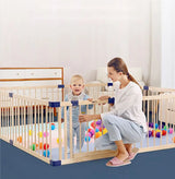 Wooden playpen with a child happily playing with colorful balls inside.