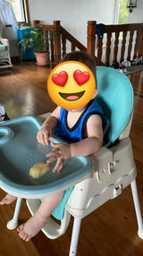 Child seated in a portable feeding high chair with a blue tray.