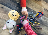 Children's hands playing with colorful pom-poms near animal-shaped containers on a wooden surface.