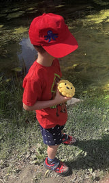 Child in a red shirt and cap holding a yellow Meli snack bowl.