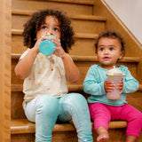 Two children sitting on a staircase holding Melii sippy cups.