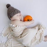Baby sleeping with a small pumpkin, wearing a knitted hat and wrapped in a beigemuslin swaddle blanket.