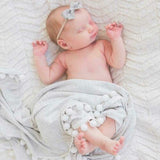 Newborn baby sleeping on a soft muslin blanket with a gray headband.