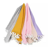 Set of five muslin swaddle in different colors with pom-pom trim .