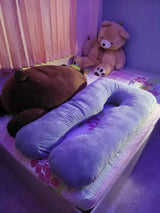 Purple U-shaped body pillow on a bed with teddy bears .