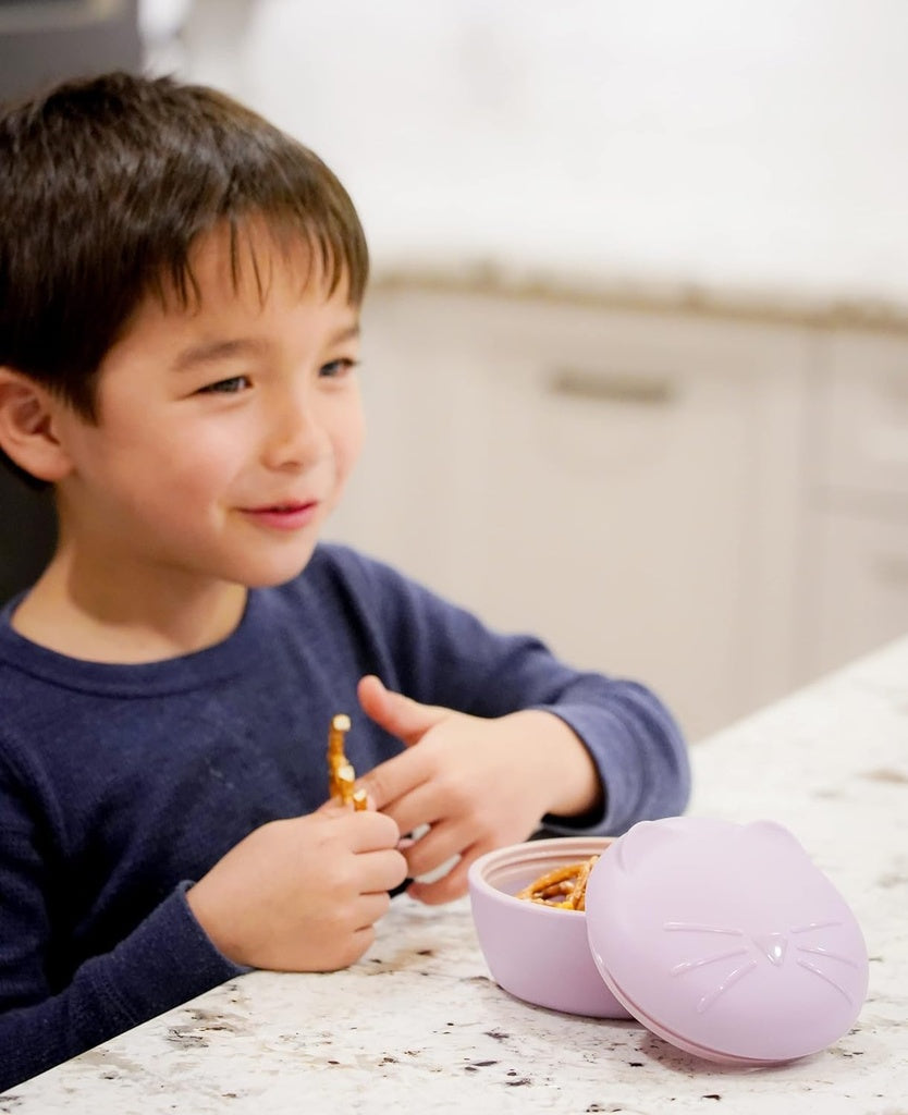 Child sitting at a table with a purple melii silicone bowl having snacks.